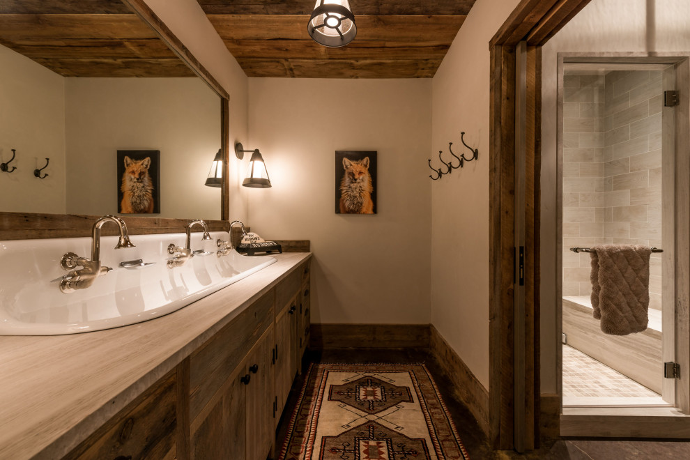 Yellowstone River Home - Example of a mountain style gray tile black floor alcove shower design with flat-panel cabinets, dark wood cabinets, beige walls, a trough sink, a hinged shower door and gray countertops