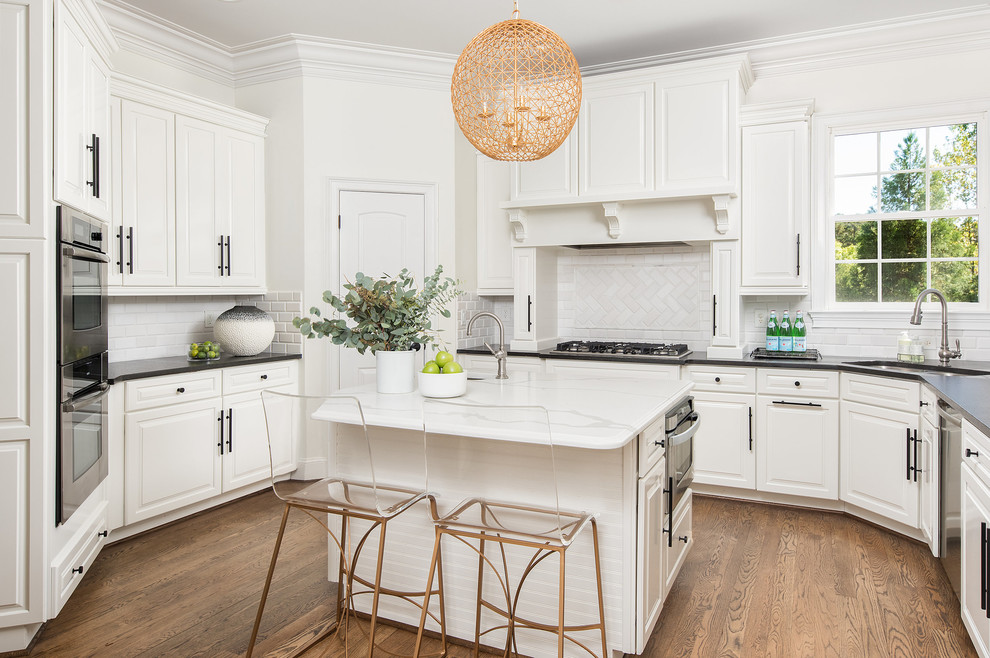 Inspiration for a transitional u-shaped kitchen in Raleigh with an undermount sink, raised-panel cabinets, white cabinets, white splashback, subway tile splashback, stainless steel appliances, medium hardwood floors, with island and brown floor.