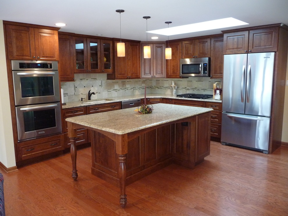 Photo of a mid-sized traditional l-shaped kitchen in Chicago with an undermount sink, raised-panel cabinets, dark wood cabinets, granite benchtops, beige splashback, ceramic splashback, stainless steel appliances, medium hardwood floors and with island.