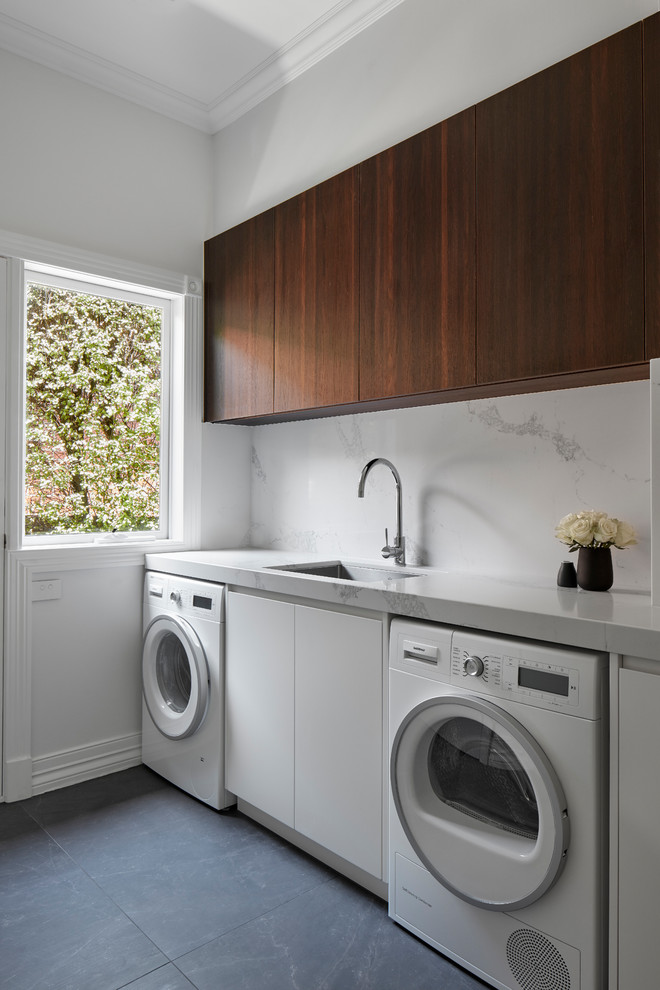 Photo of a large contemporary u-shaped laundry room in Melbourne with a double-bowl sink, flat-panel cabinets, dark wood cabinets, marble benchtops, white splashback, marble splashback, light hardwood floors and white benchtop.