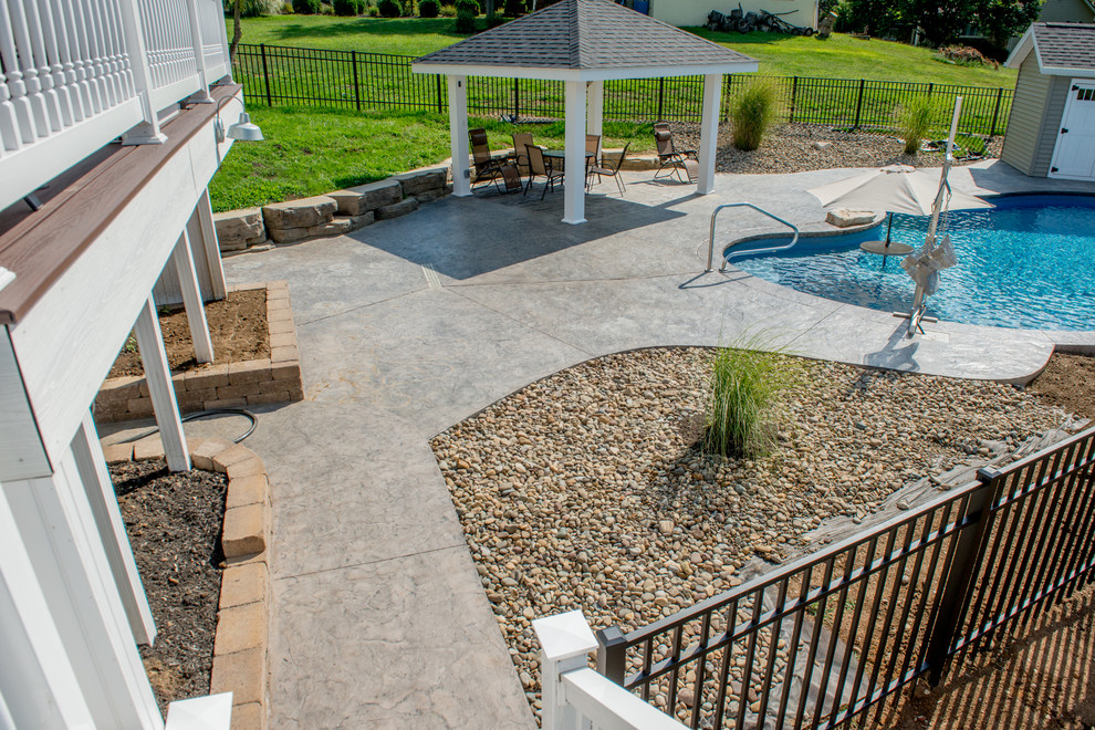 Photo of a mid-sized traditional backyard custom-shaped natural pool in Other with a water feature and stamped concrete.