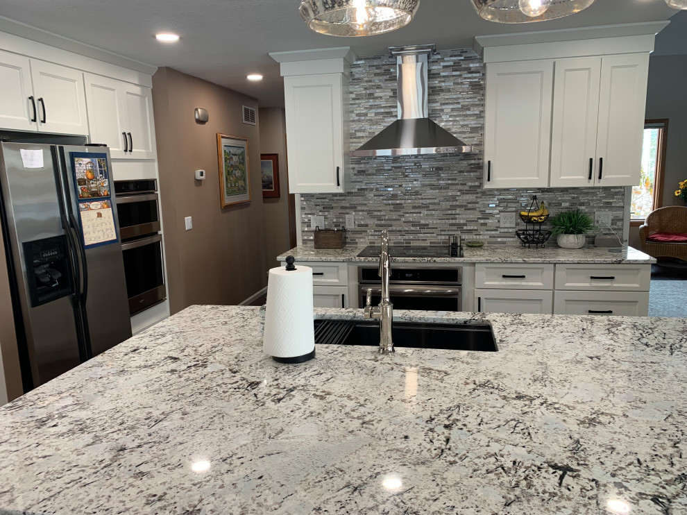 Eat-in kitchen - mid-sized transitional l-shaped eat-in kitchen idea with shaker cabinets, white cabinets, granite countertops, multicolored backsplash and an island