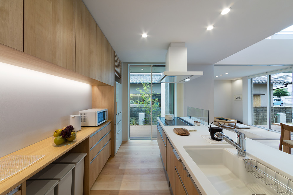 Photo of an asian galley open plan kitchen in Other with an integrated sink, flat-panel cabinets, medium wood cabinets, light hardwood floors, with island and brown floor.
