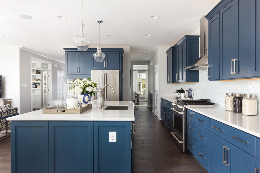 Transitional l-shaped dark wood floor and brown floor open concept kitchen photo with an undermount sink, shaker cabinets, blue cabinets, white backsplash, subway tile backsplash, stainless steel appliances, an island and white countertops