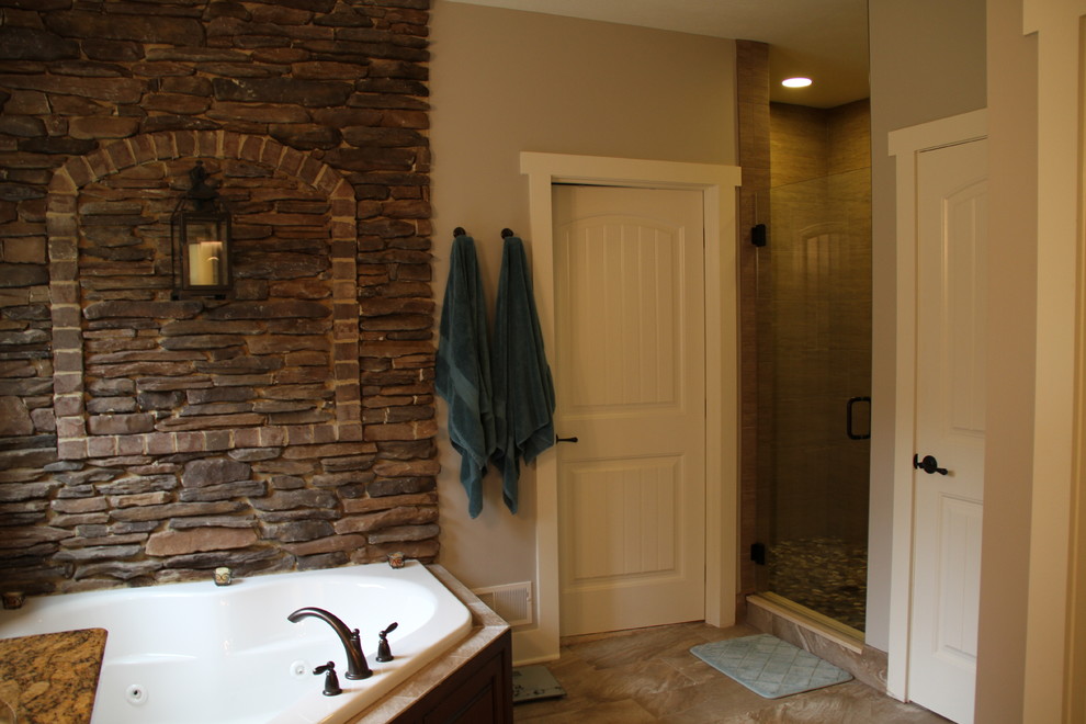 Photo of a large country master bathroom in Other with recessed-panel cabinets, dark wood cabinets, a corner tub, a corner shower, a one-piece toilet, gray tile, ceramic tile, brown walls, ceramic floors, a vessel sink and granite benchtops.