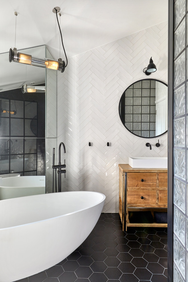 This is an example of a mid-sized contemporary master bathroom in London with furniture-like cabinets, medium wood cabinets, a freestanding tub, an open shower, a wall-mount toilet, white tile, porcelain tile, white walls, porcelain floors, a vessel sink, wood benchtops, black floor and an open shower.
