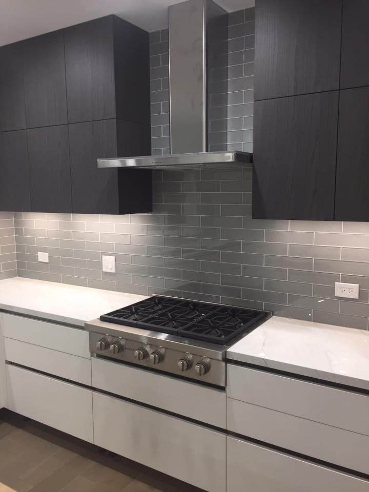 Kitchen - large transitional medium tone wood floor and brown floor kitchen idea in Chicago with an undermount sink, flat-panel cabinets, black cabinets, quartzite countertops, gray backsplash, subway tile backsplash and stainless steel appliances
