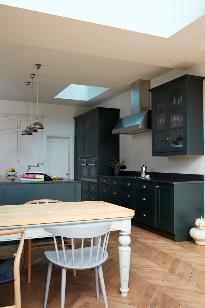 This is an example of a mid-sized traditional galley kitchen in London with medium hardwood floors, with island, beige floor and black benchtop.
