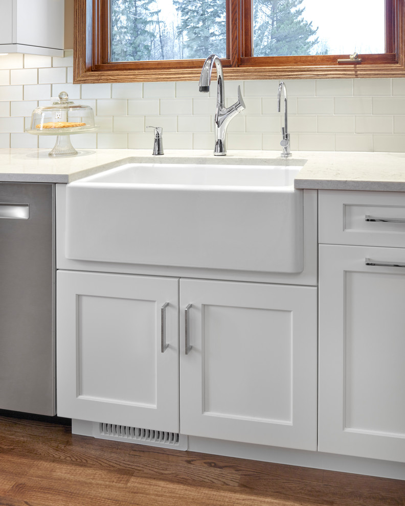 Inspiration for a mid-sized transitional l-shaped medium tone wood floor and brown floor eat-in kitchen remodel in Edmonton with a farmhouse sink, recessed-panel cabinets, white cabinets, quartz countertops, gray backsplash, glass tile backsplash, stainless steel appliances and no island