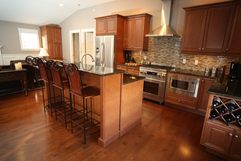 Mid-sized transitional l-shaped medium tone wood floor open concept kitchen photo in Edmonton with an undermount sink, raised-panel cabinets, medium tone wood cabinets, granite countertops, multicolored backsplash, stainless steel appliances, an island and matchstick tile backsplash
