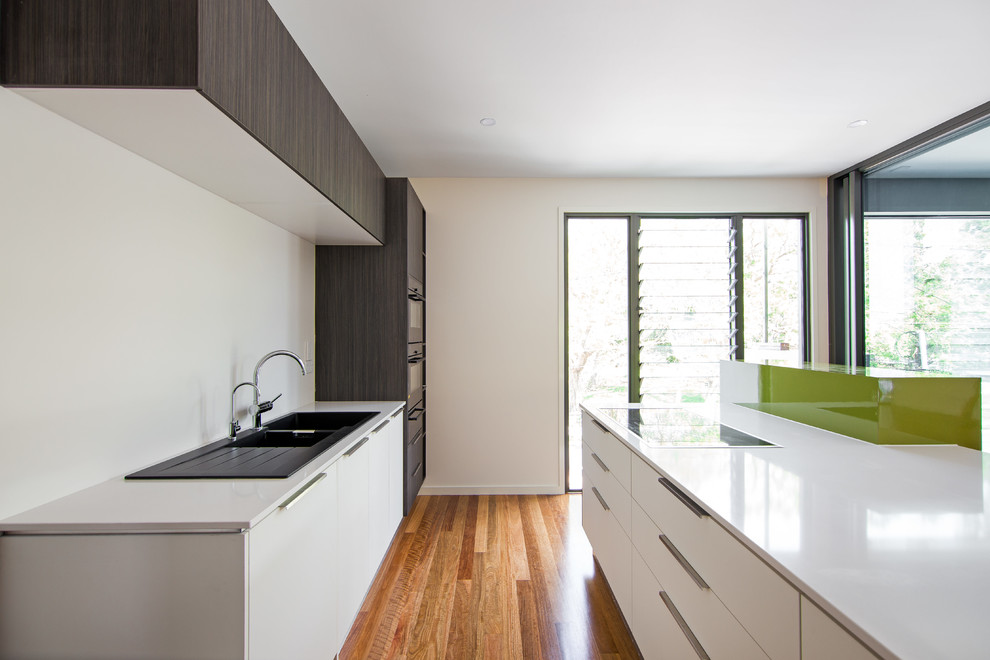 Photo of a contemporary galley kitchen in Brisbane with a double-bowl sink, stainless steel appliances, medium hardwood floors and with island.