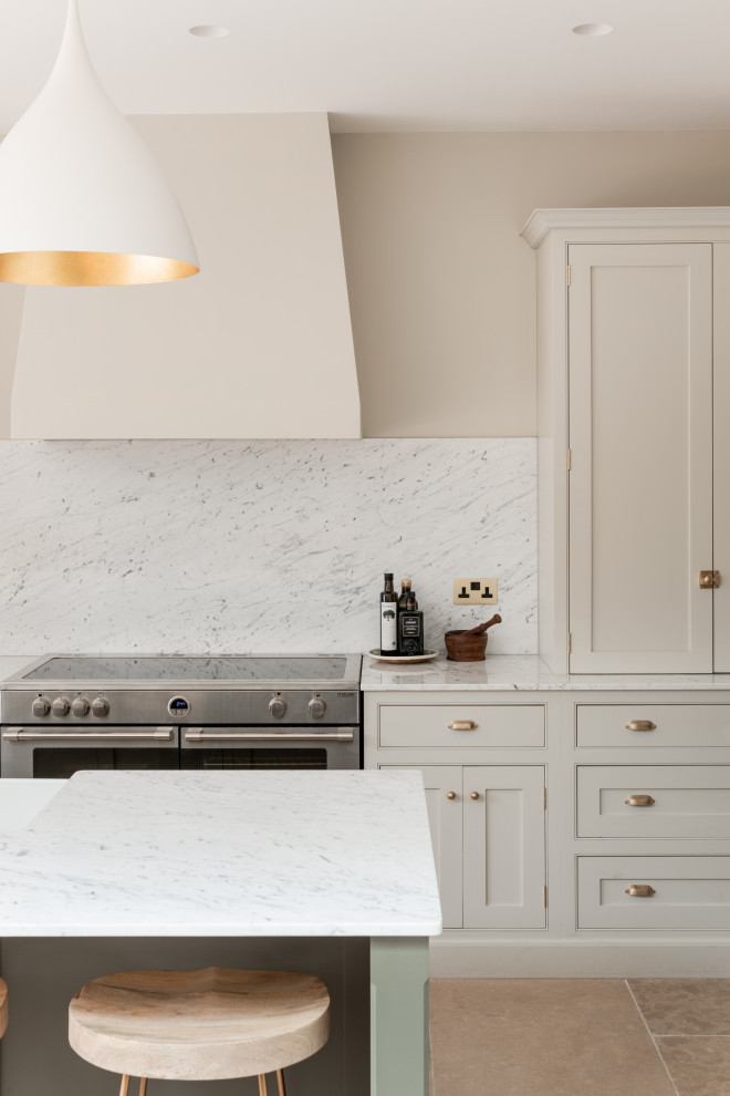 Photo of a large transitional single-wall open plan kitchen in London with a drop-in sink, shaker cabinets, light wood cabinets, marble benchtops, white splashback, marble splashback, black appliances, limestone floors, with island, beige floor, white benchtop and vaulted.