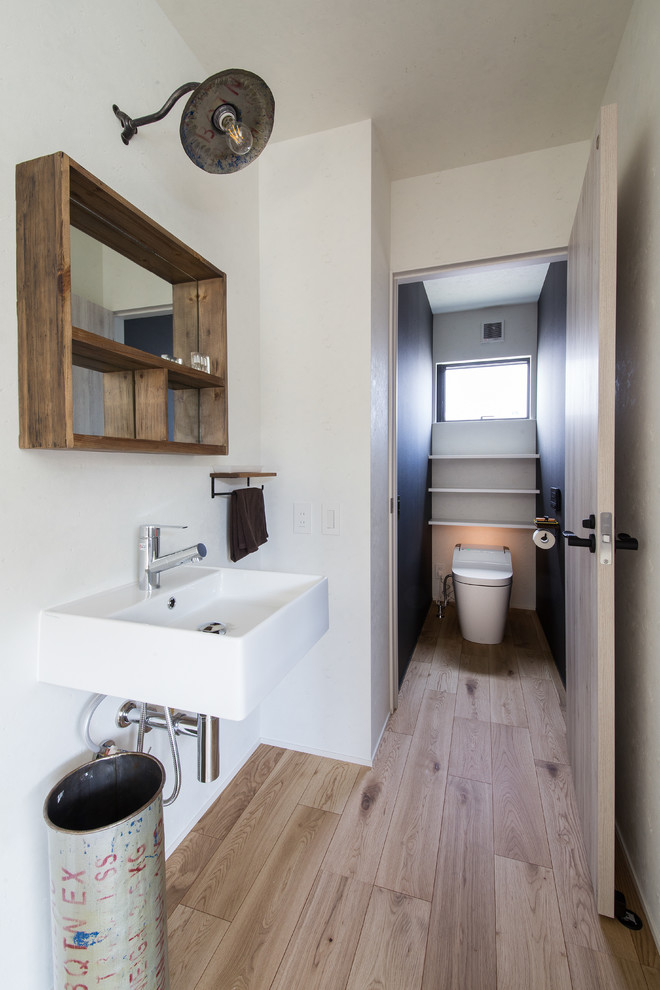 This is an example of an industrial powder room in Other with white walls, light hardwood floors, a wall-mount sink and beige floor.