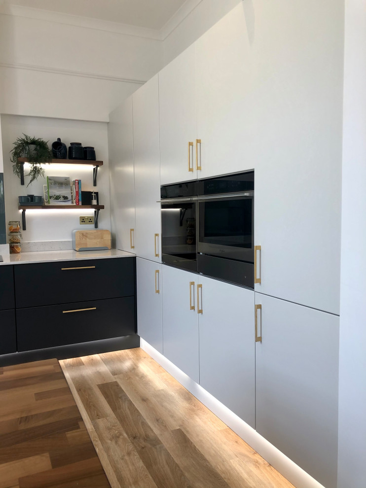 This is an example of a mid-sized modern galley open plan kitchen in Glasgow with an integrated sink, flat-panel cabinets, grey cabinets, quartzite benchtops, blue splashback, glass sheet splashback, stainless steel appliances, medium hardwood floors, a peninsula, brown floor and white benchtop.