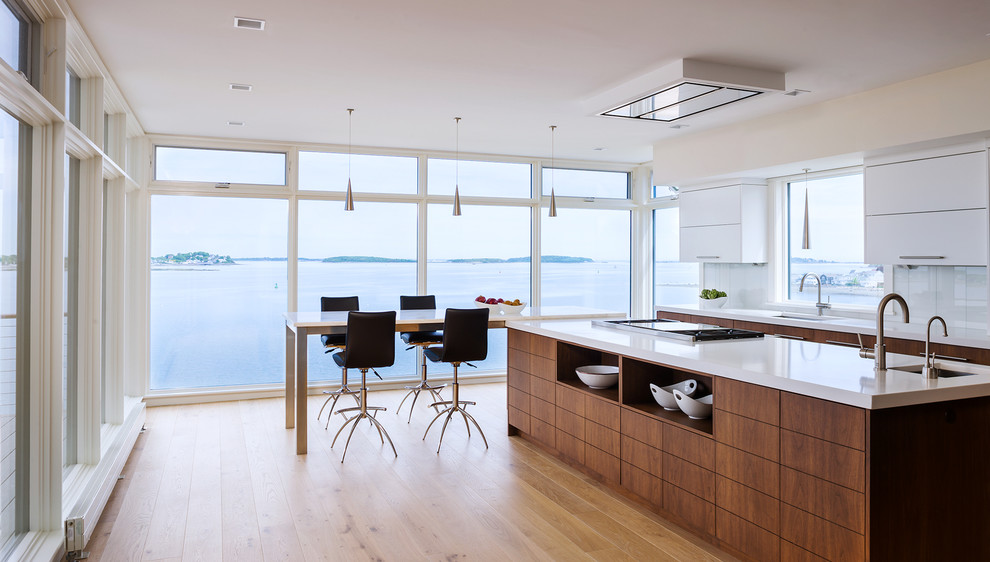 Photo of a contemporary eat-in kitchen in Boston with an undermount sink, flat-panel cabinets, white cabinets, white splashback, light hardwood floors, with island and glass sheet splashback.