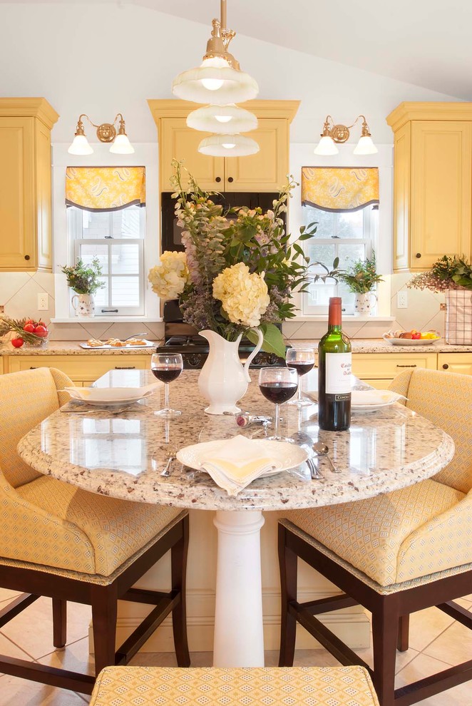 Example of a classic porcelain tile eat-in kitchen design in Philadelphia with an undermount sink, raised-panel cabinets, yellow cabinets, granite countertops, beige backsplash, porcelain backsplash, paneled appliances and an island