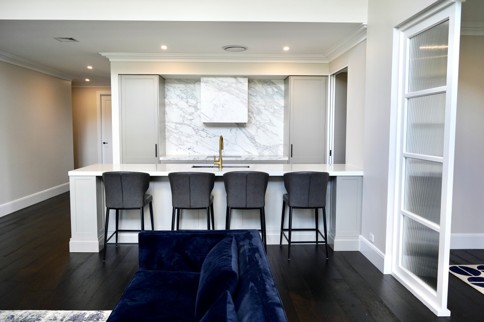 Large transitional single-wall open plan kitchen in Sydney with an undermount sink, shaker cabinets, grey cabinets, marble benchtops, white splashback, marble splashback, black appliances, dark hardwood floors, with island, brown floor and white benchtop.