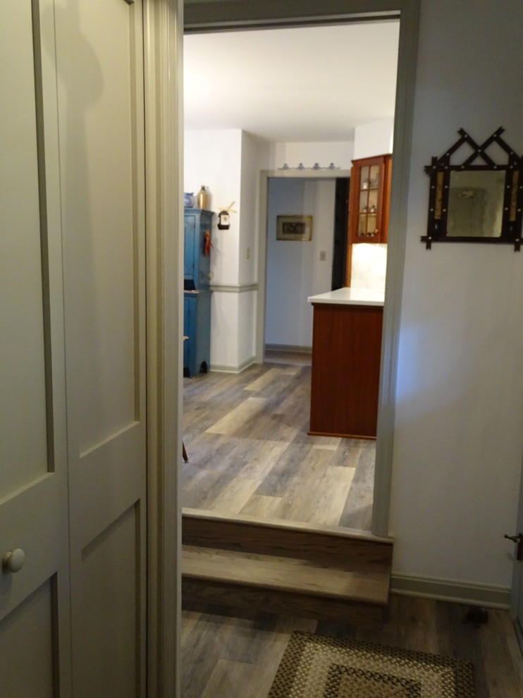 Example of a mid-sized classic u-shaped laminate floor and multicolored floor enclosed kitchen design with an undermount sink, shaker cabinets, medium tone wood cabinets, quartz countertops, beige backsplash, ceramic backsplash, black appliances, white countertops and a peninsula