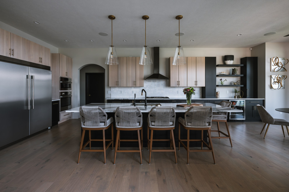 Inspiration for a transitional l-shaped medium tone wood floor and brown floor kitchen remodel with an undermount sink, flat-panel cabinets, black cabinets, white backsplash, stainless steel appliances, an island and white countertops