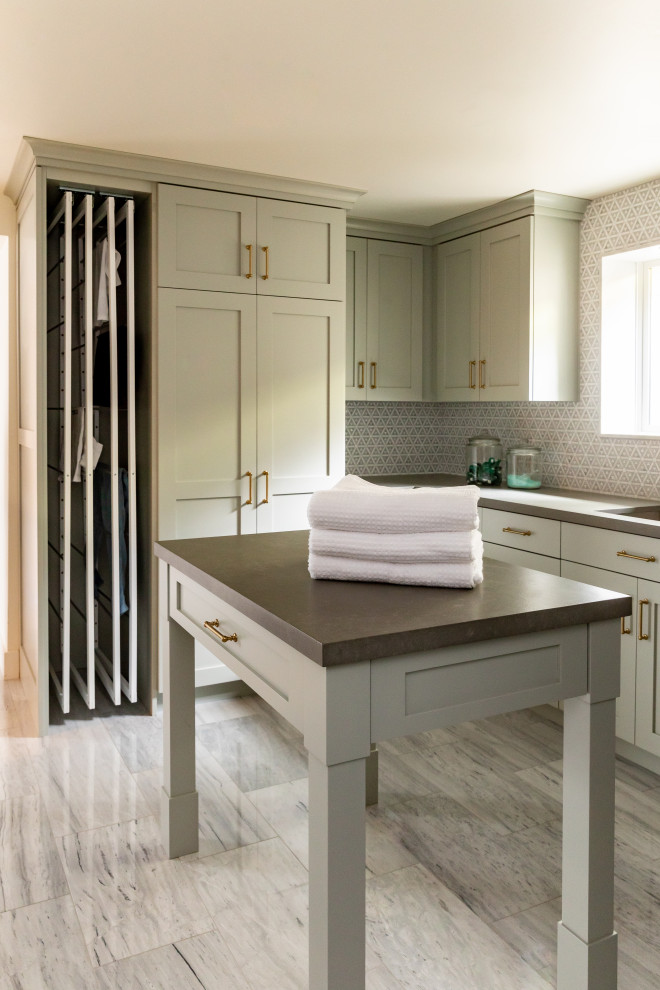 Inredning av en stor grå u-formad grått tvättstuga enbart för tvätt och med garderob, med en undermonterad diskho, skåp i shakerstil, gröna skåp, bänkskiva i kvartsit, stänkskydd i mosaik, marmorgolv och grått golv