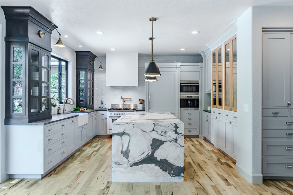 Inspiration for a mid-sized transitional u-shaped kitchen in Denver with a farmhouse sink, shaker cabinets, grey cabinets, white splashback, panelled appliances, light hardwood floors, with island and beige floor.