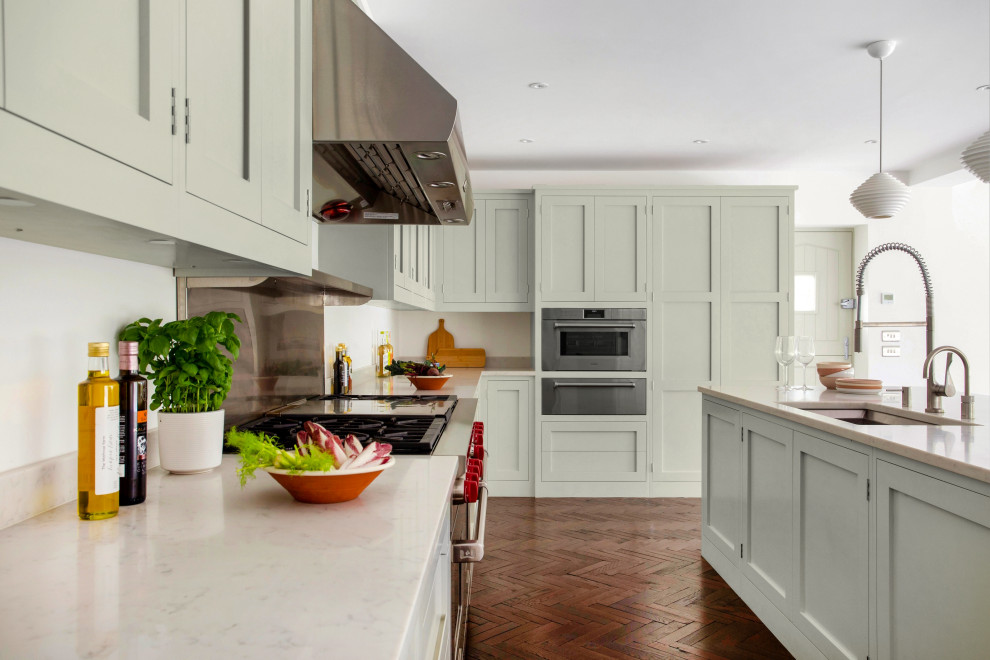 Design ideas for a large classic u-shaped open plan kitchen in London with a submerged sink, shaker cabinets, green cabinets, quartz worktops, stainless steel appliances, medium hardwood flooring, an island, brown floors and white worktops.