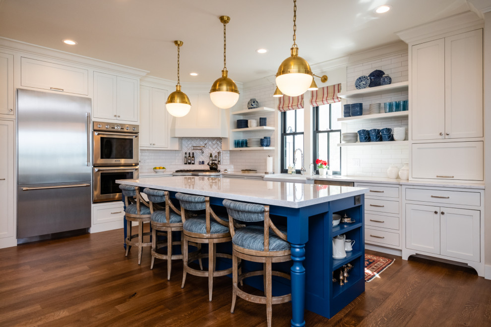 Inspiration for a transitional u-shaped kitchen in Minneapolis with a farmhouse sink, shaker cabinets, white cabinets, white splashback, subway tile splashback, stainless steel appliances, medium hardwood floors, with island, brown floor and white benchtop.