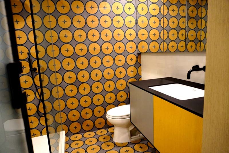 This is an example of a mid-sized modern 3/4 bathroom in Los Angeles with flat-panel cabinets, orange cabinets, a corner shower, a two-piece toilet, orange tile, ceramic tile, orange walls, ceramic floors, a drop-in sink, engineered quartz benchtops, orange floor, a hinged shower door, black benchtops, a niche, a single vanity and a built-in vanity.