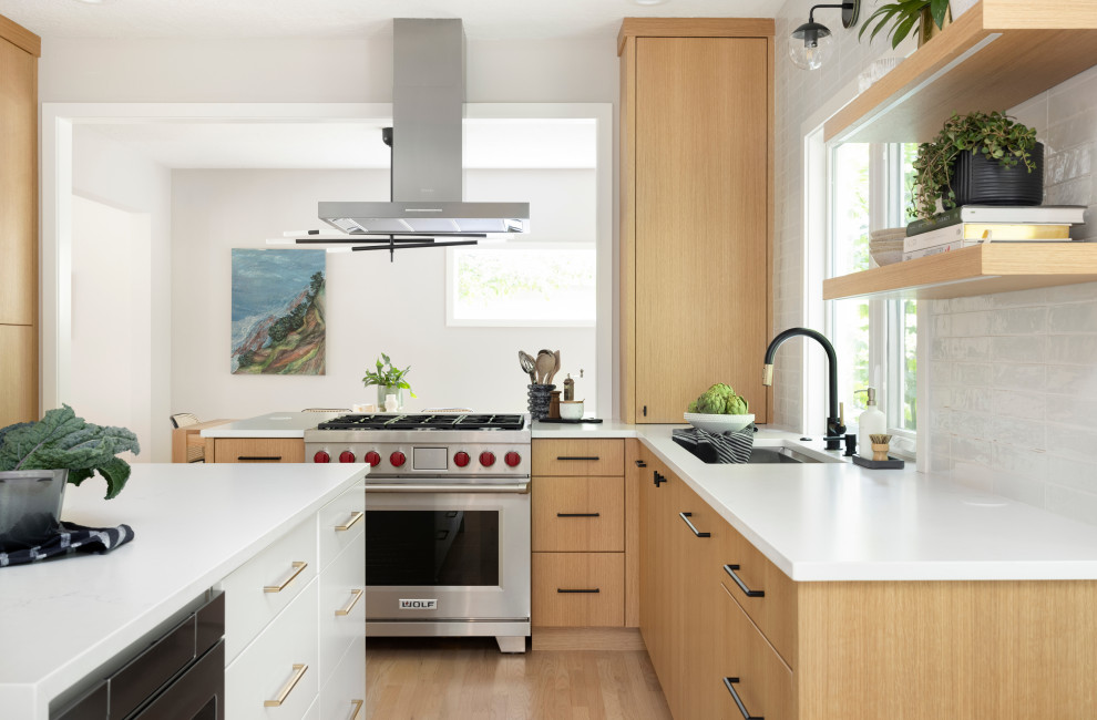 Inspiration for a mid-sized contemporary u-shaped open plan kitchen in Portland with an undermount sink, flat-panel cabinets, medium wood cabinets, quartz benchtops, white splashback, cement tile splashback, stainless steel appliances, light hardwood floors, with island and white benchtop.
