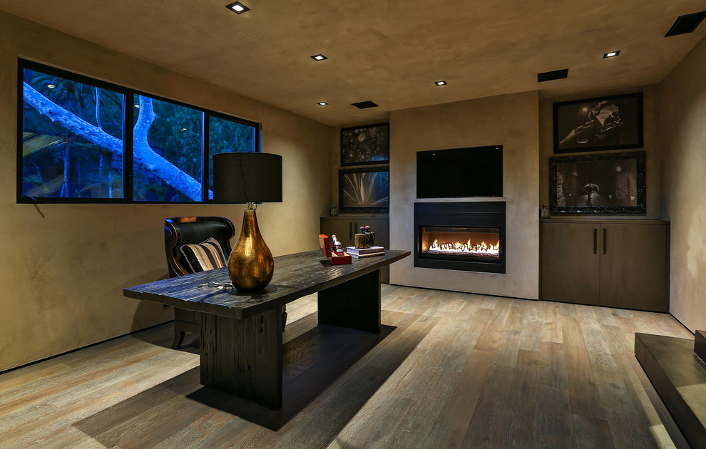 Mid-sized contemporary study room in Los Angeles with beige walls, light hardwood floors, a ribbon fireplace, a freestanding desk, a concrete fireplace surround and brown floor.