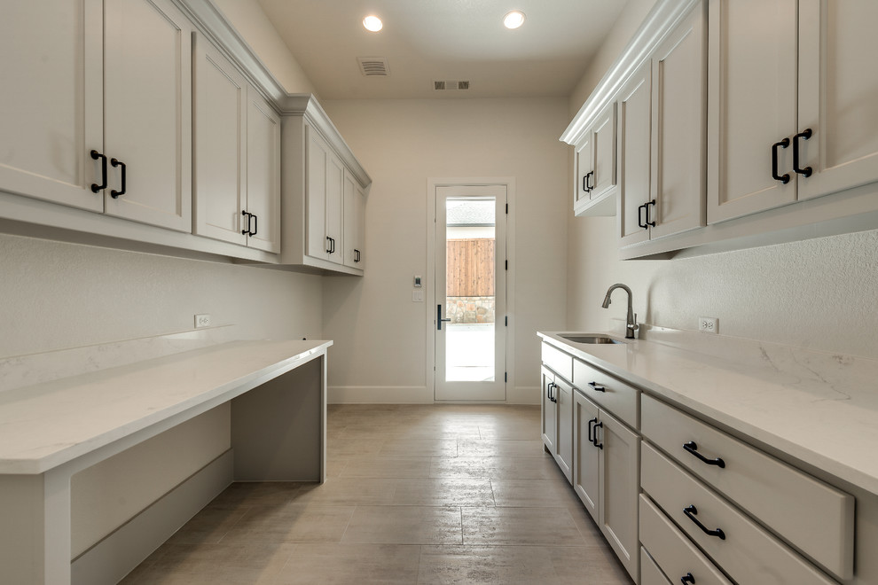 Design ideas for a large transitional galley dedicated laundry room in Dallas with an utility sink, flat-panel cabinets, grey cabinets, quartz benchtops, beige walls, ceramic floors, a side-by-side washer and dryer, beige floor and white benchtop.