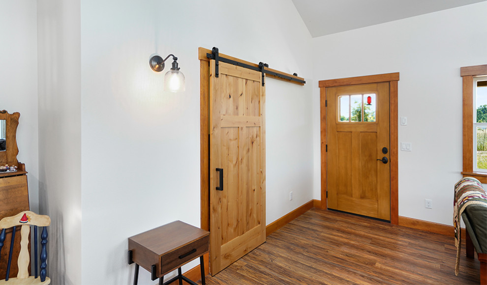 Example of a large mountain style medium tone wood floor, brown floor and vaulted ceiling foyer design with white walls and a medium wood front door