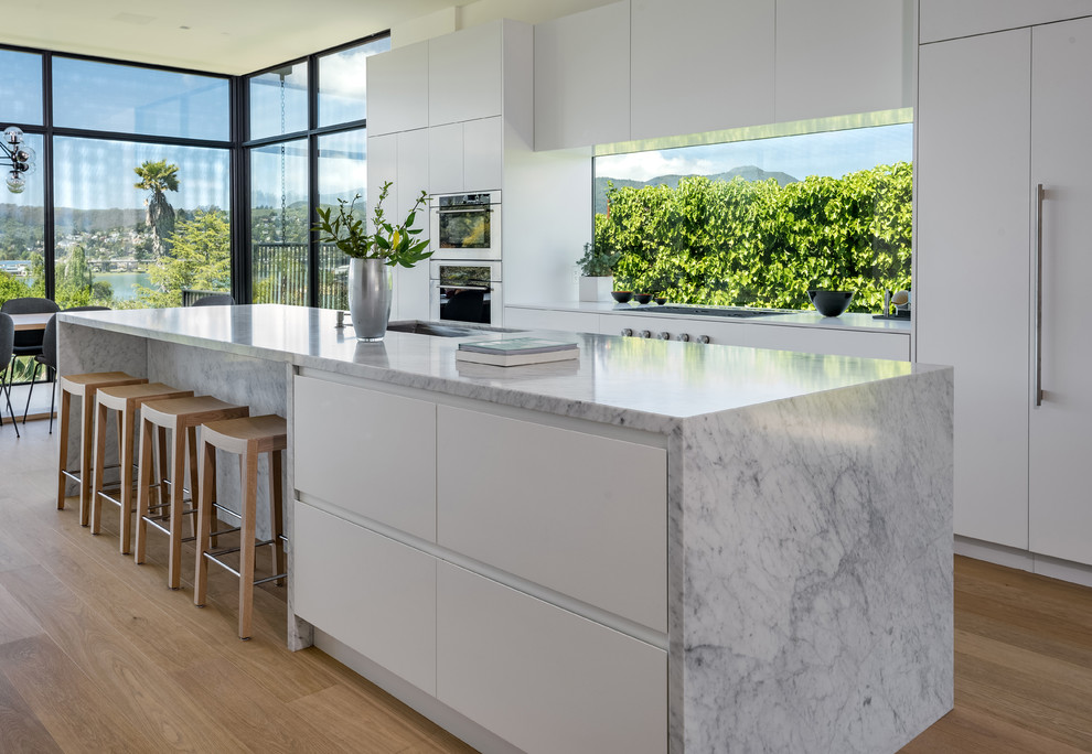 Design ideas for a large contemporary galley open plan kitchen in San Francisco with an undermount sink, flat-panel cabinets, white cabinets, marble benchtops, with island, window splashback, panelled appliances, medium hardwood floors, brown floor and grey benchtop.
