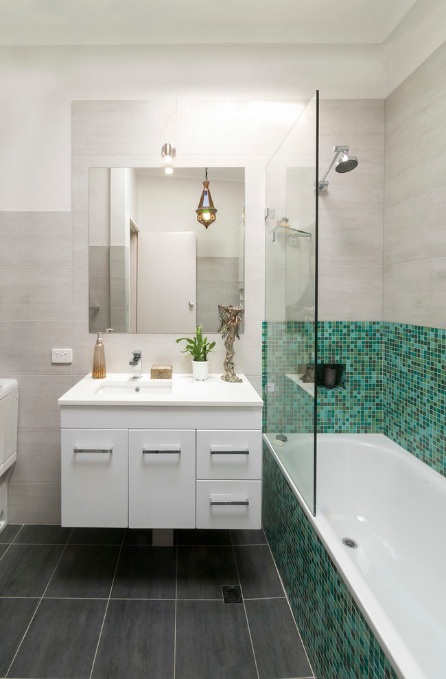 Inspiration for a mid-sized contemporary bathroom in Canberra - Queanbeyan with an undermount sink, flat-panel cabinets, white cabinets, engineered quartz benchtops, a drop-in tub, a shower/bathtub combo, a one-piece toilet, multi-coloured tile, mosaic tile and ceramic floors.