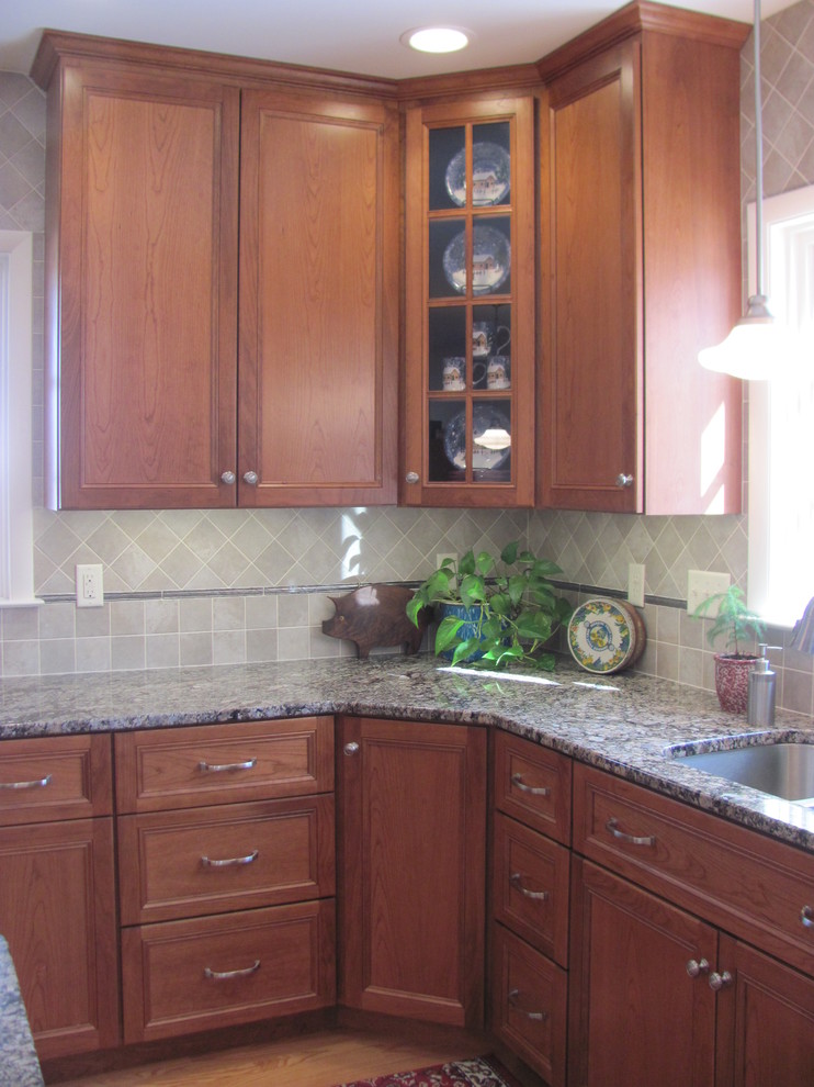 Example of a large classic single-wall light wood floor home design design with a drop-in sink, raised-panel cabinets, medium tone wood cabinets, granite countertops, gray backsplash, porcelain backsplash, stainless steel appliances and an island