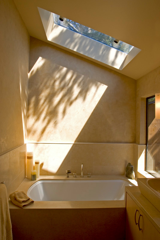 Design ideas for a mid-sized contemporary master bathroom in San Francisco with flat-panel cabinets, beige cabinets, a drop-in tub, a curbless shower, a one-piece toilet, beige tile, limestone, yellow walls, limestone floors, a vessel sink, limestone benchtops, yellow floor, a hinged shower door and beige benchtops.