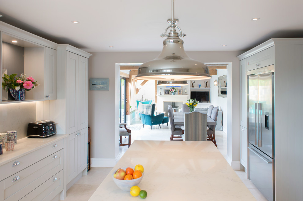 Inspiration for a mid-sized contemporary u-shaped open plan kitchen in Cornwall with a farmhouse sink, shaker cabinets, grey cabinets, quartzite benchtops, white splashback, ceramic splashback, stainless steel appliances, limestone floors, with island, beige floor and white benchtop.