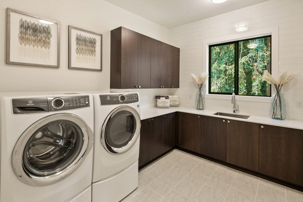 Photo of a large modern l-shaped dedicated laundry room in Seattle with an undermount sink, flat-panel cabinets, dark wood cabinets, quartz benchtops, white splashback, ceramic splashback, white walls, ceramic floors, a side-by-side washer and dryer, grey floor and white benchtop.