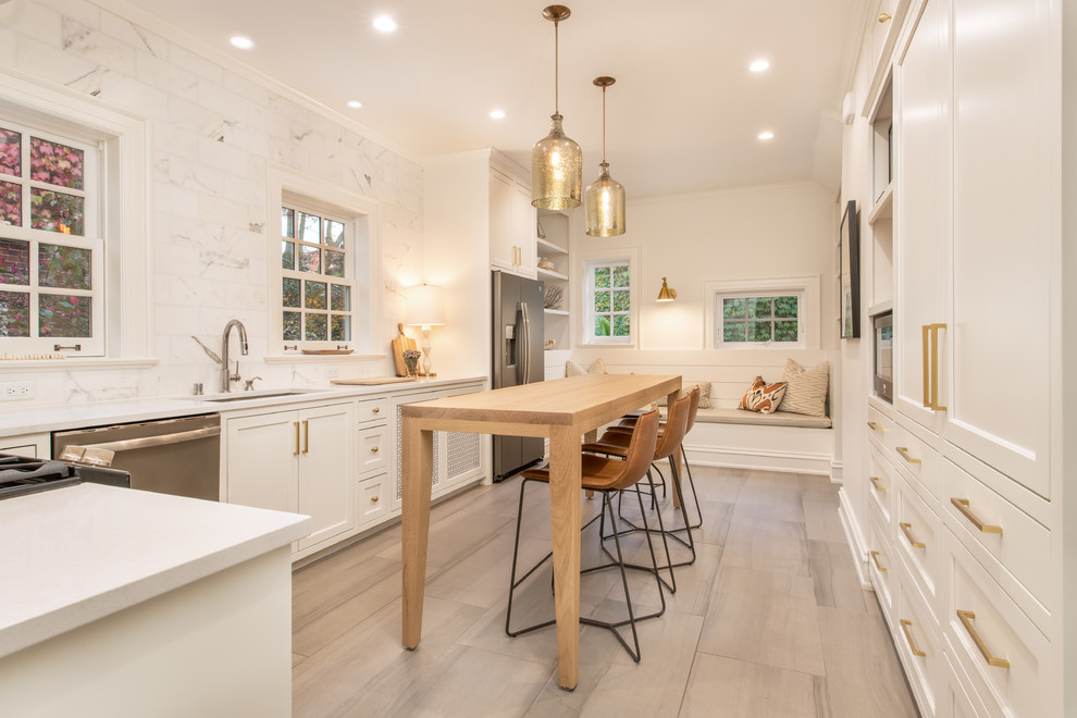 This is an example of a transitional u-shaped separate kitchen in Milwaukee with an undermount sink, shaker cabinets, white cabinets, white splashback, marble splashback, stainless steel appliances, with island and grey floor.