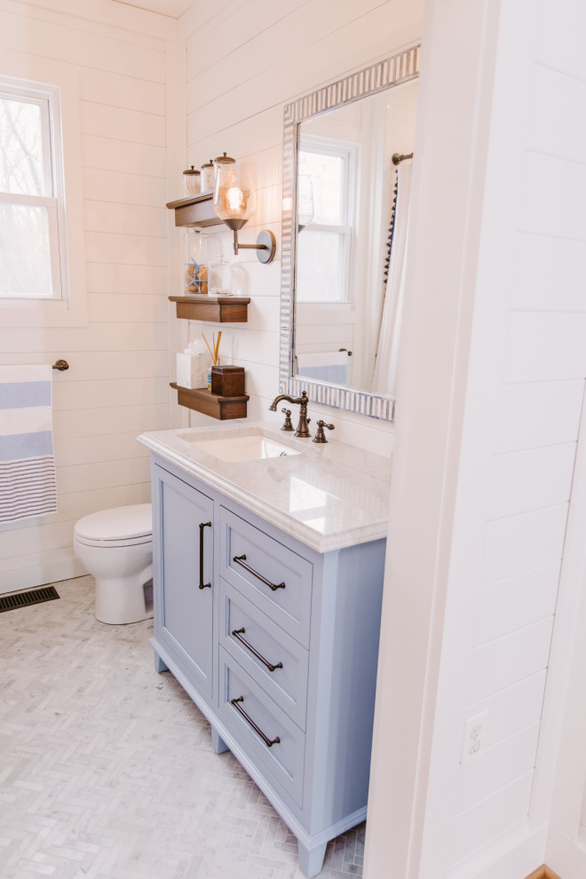 Design ideas for a small beach style kids bathroom in Baltimore with beaded inset cabinets, blue cabinets, an alcove tub, an alcove shower, a one-piece toilet, white tile, subway tile, white walls, marble floors, a drop-in sink, engineered quartz benchtops, grey floor, a shower curtain, white benchtops, a single vanity, a built-in vanity and planked wall panelling.