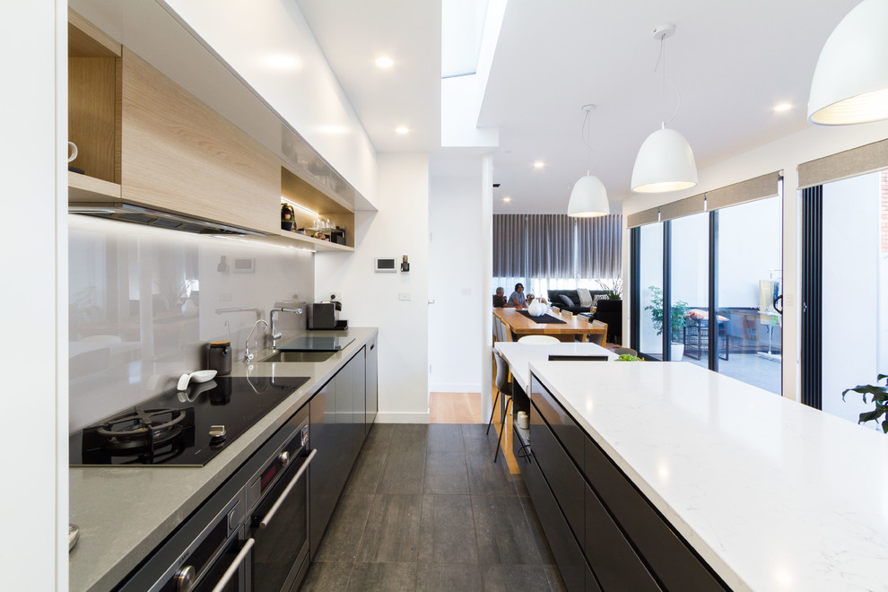 This is an example of a mid-sized contemporary galley open plan kitchen in Melbourne with an undermount sink, flat-panel cabinets, white cabinets, quartz benchtops, white splashback, glass sheet splashback, stainless steel appliances, medium hardwood floors, with island, brown floor and white benchtop.