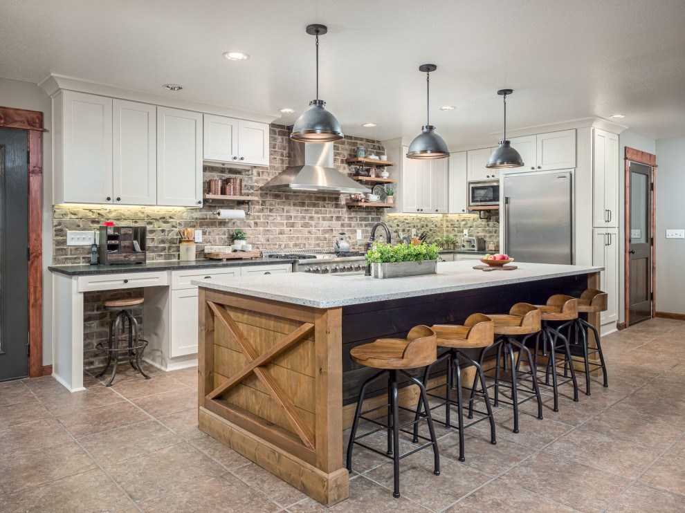 Inspiration for a country l-shaped kitchen in Atlanta with a farmhouse sink, shaker cabinets, white cabinets, grey splashback, brick splashback, stainless steel appliances, with island, beige floor and black benchtop.