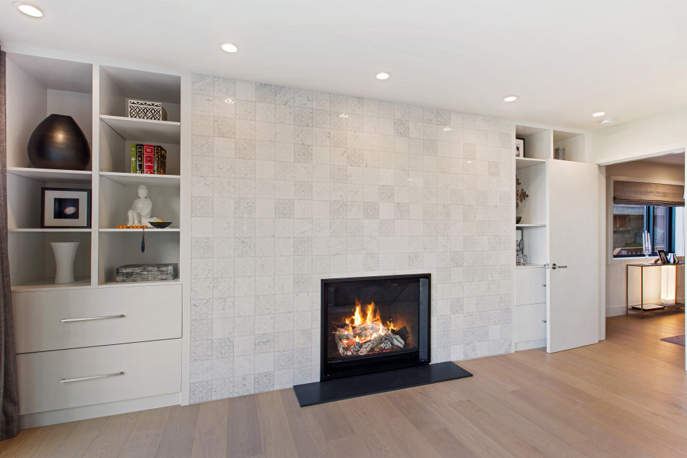 This is an example of a large modern master bedroom in San Francisco with white walls, light hardwood floors, a tile fireplace surround and beige floor.