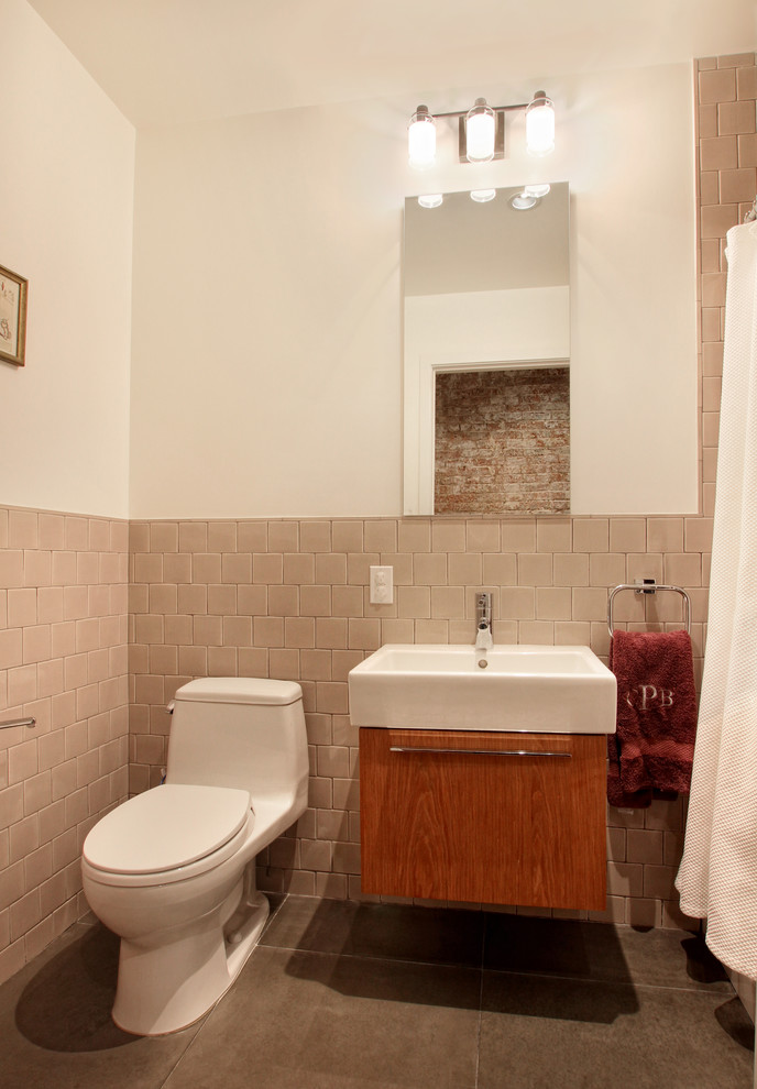 Photo of a small contemporary master bathroom in New York with flat-panel cabinets, medium wood cabinets, an alcove tub, a shower/bathtub combo, a one-piece toilet, beige tile, white walls, porcelain floors, a vessel sink, solid surface benchtops and ceramic tile.