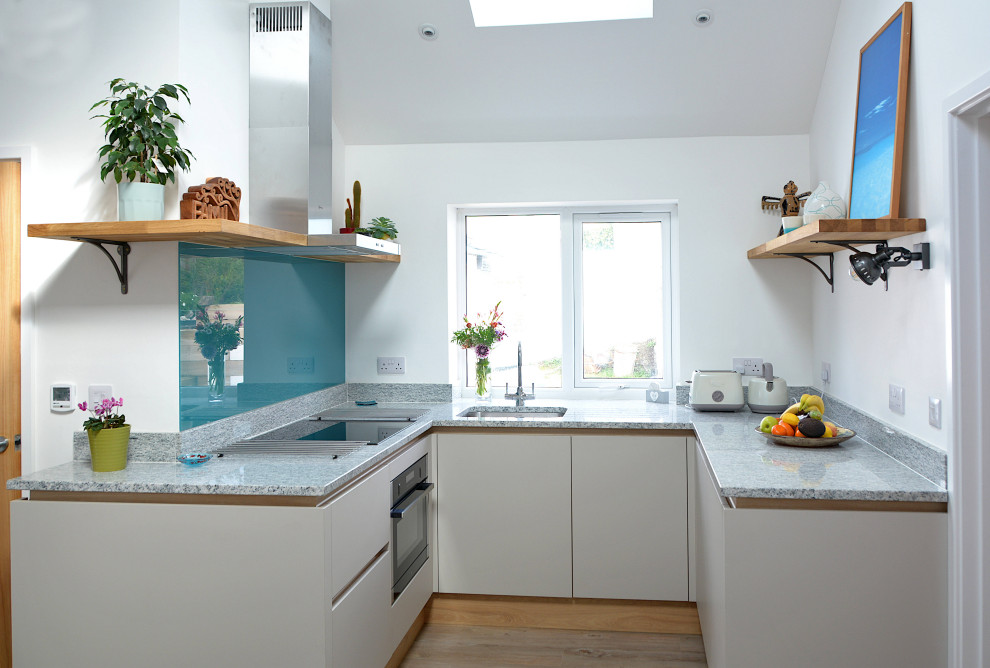Inspiration for a small contemporary u-shaped kitchen in Cornwall with flat-panel cabinets, grey cabinets, quartzite benchtops, blue splashback, glass sheet splashback, black appliances, vinyl floors, no island, brown floor, grey benchtop and an undermount sink.