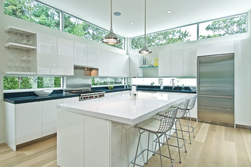 Photo of a contemporary l-shaped kitchen in New York with flat-panel cabinets, white cabinets, light hardwood floors and with island.