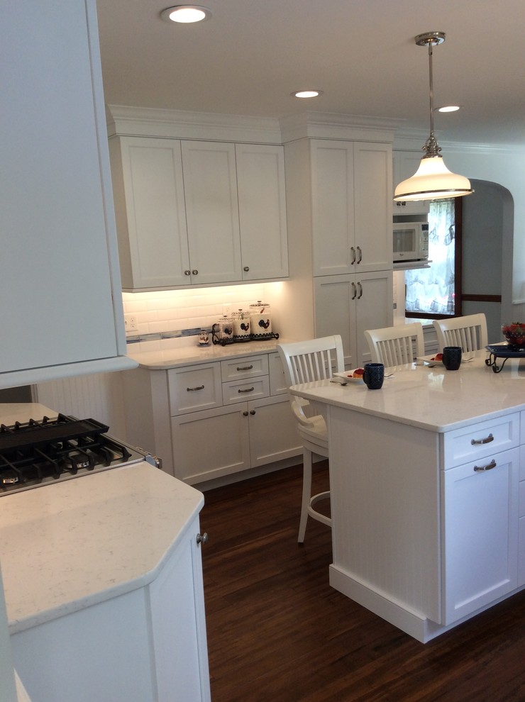 Photo of a mid-sized country u-shaped eat-in kitchen in Other with a farmhouse sink, shaker cabinets, white cabinets, quartz benchtops, white splashback, porcelain splashback, stainless steel appliances, bamboo floors and with island.