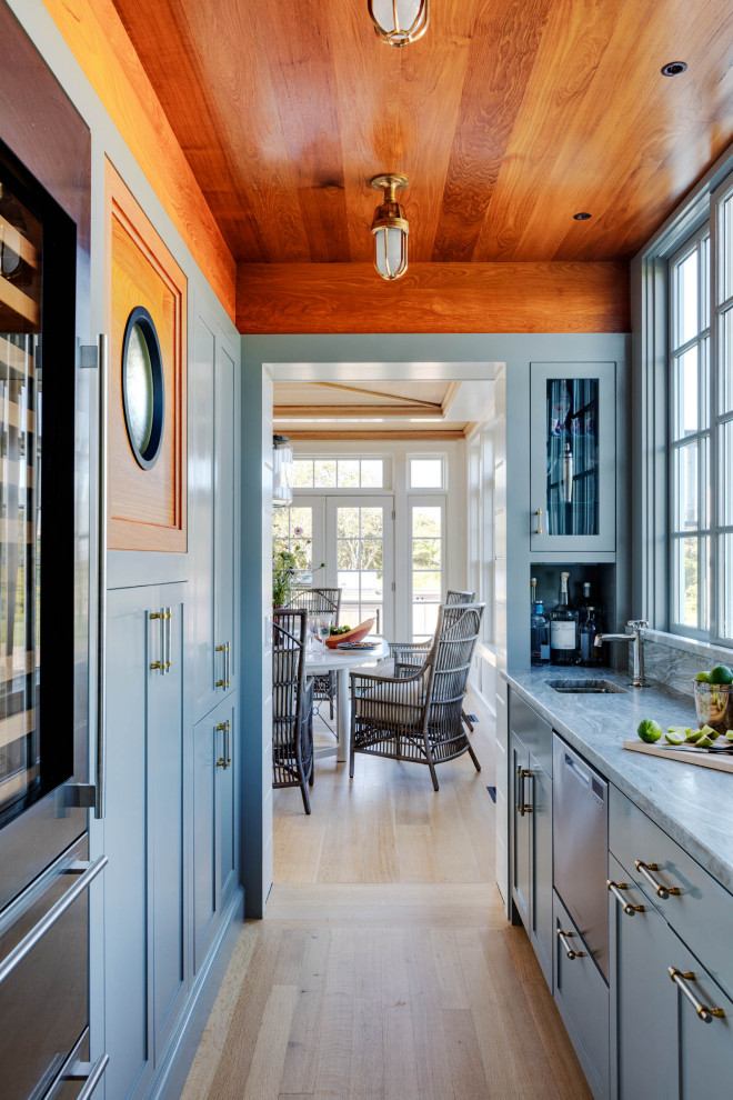 Beach style galley home bar in Boston with an undermount sink, shaker cabinets, blue cabinets, light hardwood floors, beige floor and grey benchtop.