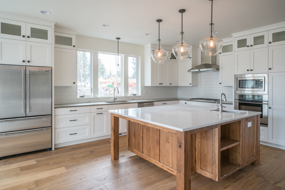 Example of a mid-sized transitional l-shaped medium tone wood floor eat-in kitchen design with an undermount sink, shaker cabinets, white cabinets, quartz countertops, white backsplash, subway tile backsplash, stainless steel appliances and an island