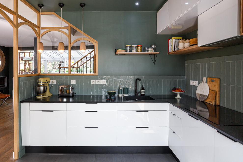 Inspiration for a mid-sized scandinavian l-shaped ceramic tile and gray floor enclosed kitchen remodel in Paris with an undermount sink, flat-panel cabinets, white cabinets, granite countertops, green backsplash, ceramic backsplash, paneled appliances, no island and black countertops